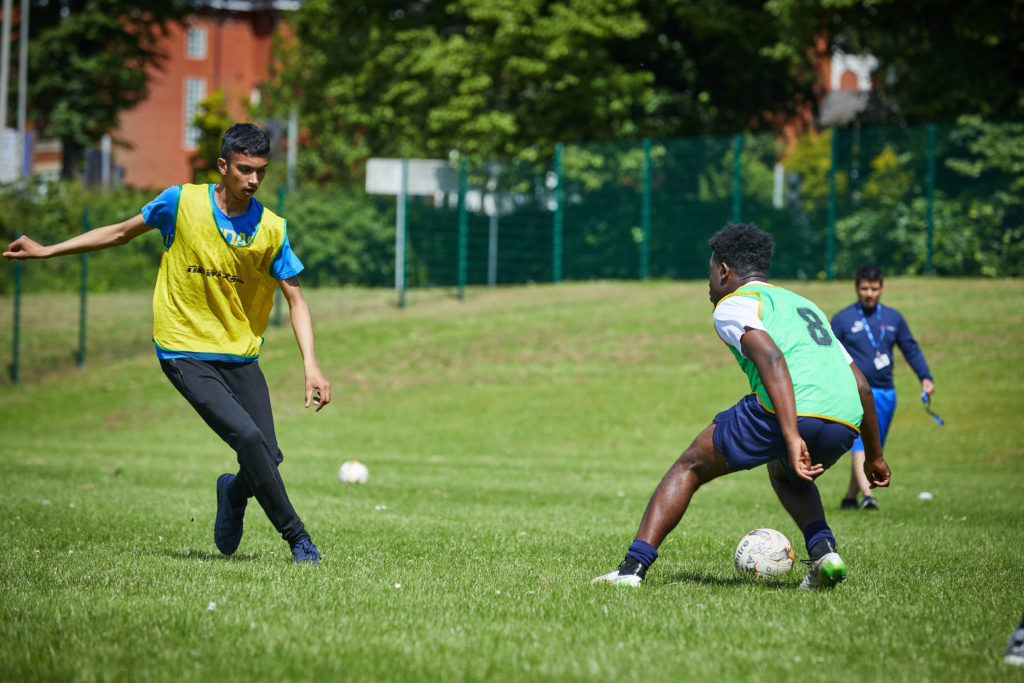 photo of males playing football outside on pitch
