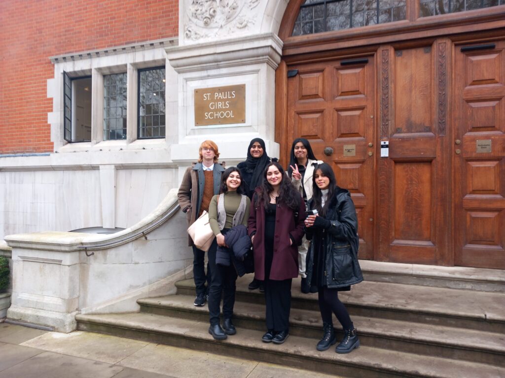 Six students smile and pose on steps outside St Pauls Girls School, with a sign visible on the wall.