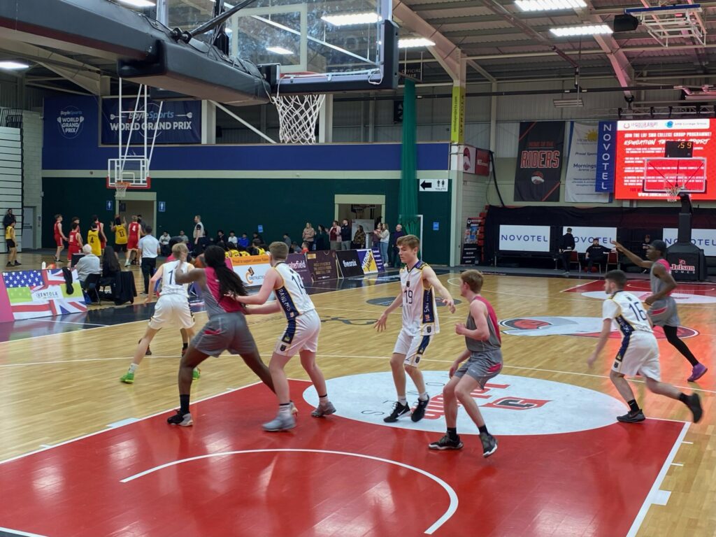 A youth basketball game in progress, with players defending near the hoop in an indoor gym.