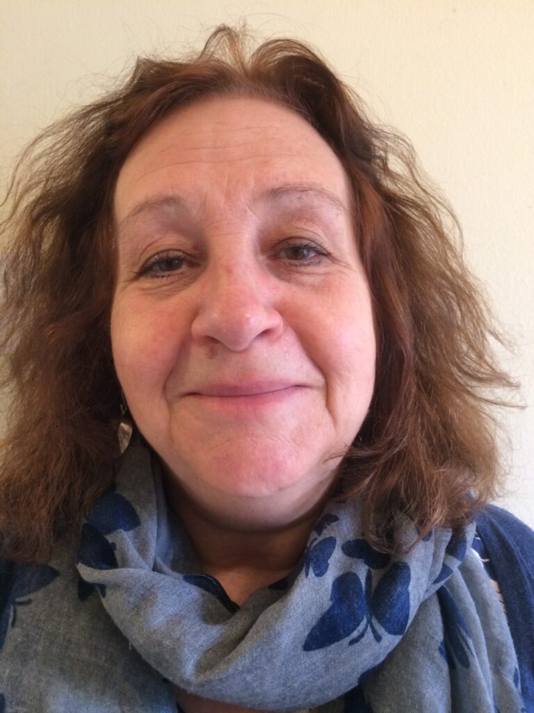 A middle-aged woman with wavy brown hair, smiling softly, wearing a blue scarf with a butterfly pattern.