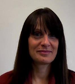 Woman with straight dark hair and bangs, wearing a maroon top, smiling slightly against a plain background.
