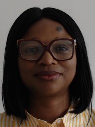 A woman with straight black hair and large glasses, wearing a yellow and white striped shirt, smiles gently.