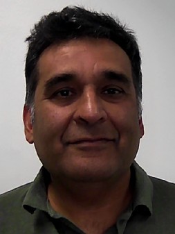 A man with dark hair and a slight smile faces the camera against a plain, light-colored background.