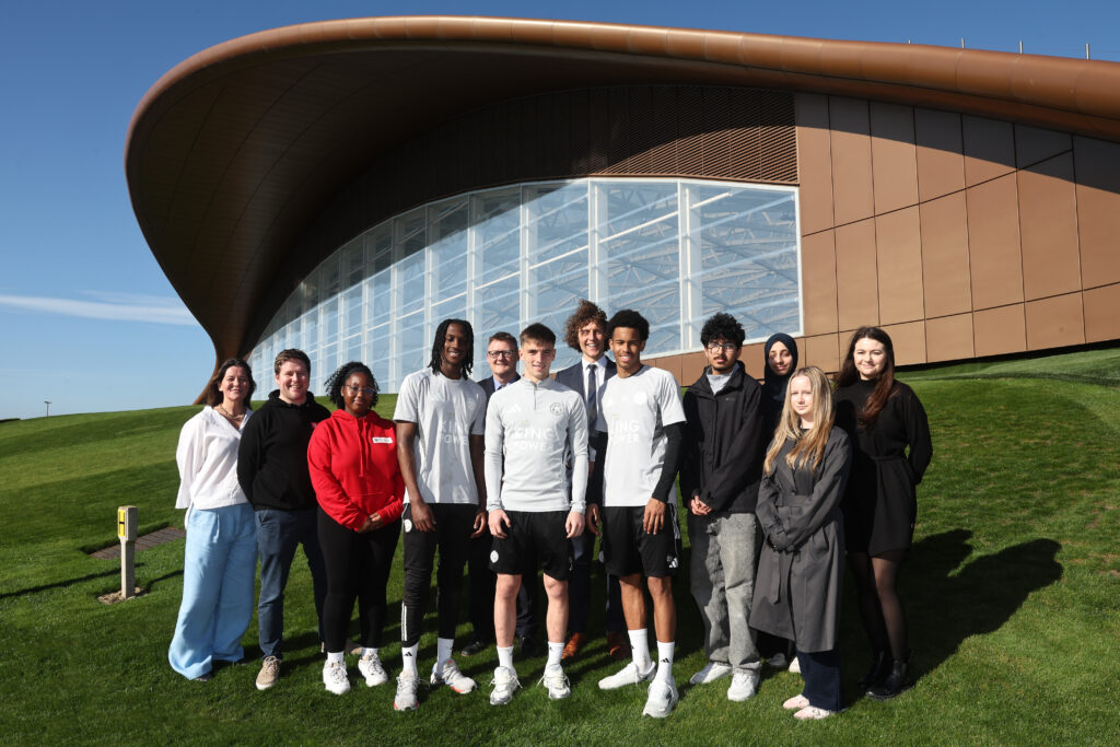 A group of people posing together outside a modern building with a curved roof on a sunny day.
