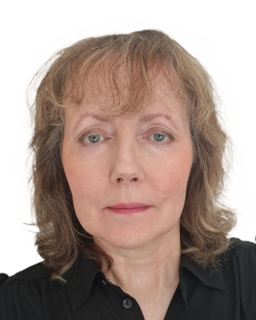A woman with light brown hair and a black top looks at the camera with a neutral expression.