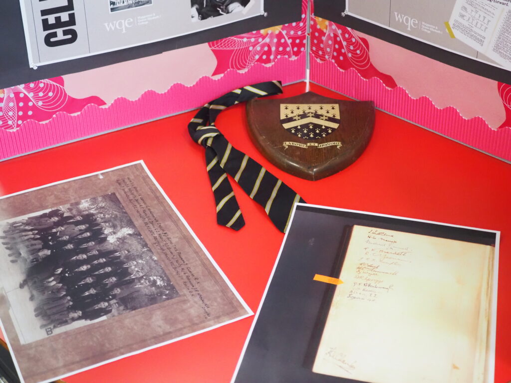 A striped tie, a wooden shield plaque, and two vintage documents displayed on a red surface.